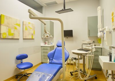 A clean dental office with a blue patient chair, modern equipment, and two abstract art pieces on the wall.