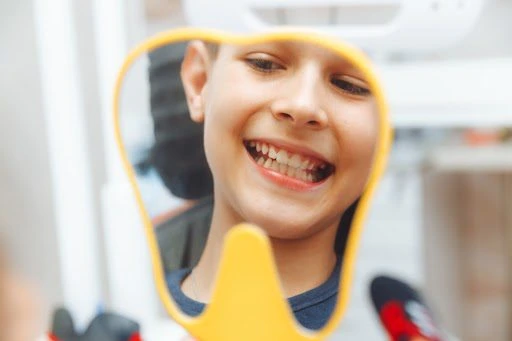 A smiling child looks into a tooth-shaped mirror during a dental checkup, happily examining their clean teeth.